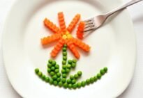 A playful flower made from carrots and peas on a white plate with a fork, showcasing creativity in food art.